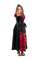 A full-length shot of a Blonde child dressed as a vampire for halloween holidays making stop gesture with her hand isolated on white