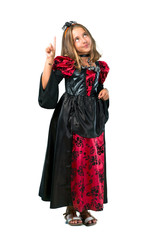 Fototapeta premium A full-length shot of a Blonde child dressed as a vampire for halloween holidays counting number one sign isolated on white