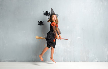 Little girl dressed as a witch for halloween holidays above on the broom and flying