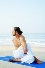 Fototapeta na wymiar Athletic Man on Mat doing Yoga at the Beach