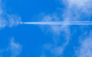 A jet flies across a blue cloudy sky leaving vapour trails