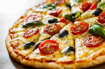 sliced Pizza Margherita or Margarita with Mozzarella cheese, tomato, olive. Italian pizza on wooden background