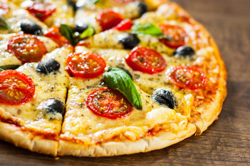 sliced Pizza Margherita or Margarita with Mozzarella cheese, tomato, olive. Italian pizza on wooden background