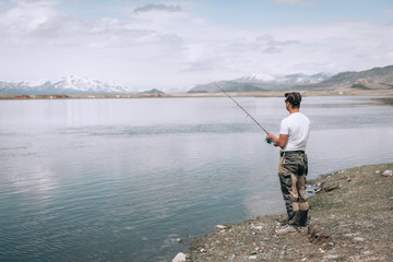 The guy fishing on the shore of a mountain lake . Reflection of mountains in water