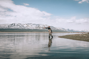 Fototapeta premium The guy fishing on the shore of a mountain lake . Reflection of mountains in water