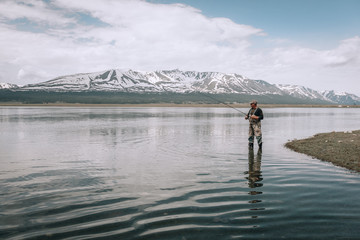 The guy fishing on the shore of a mountain lake . Reflection of mountains in water