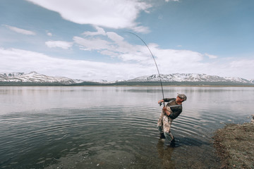 The guy fishing on the shore of a mountain lake . Reflection of mountains in water