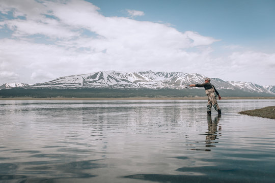The guy fishing on the shore of a mountain lake . Reflection of mountains in water
