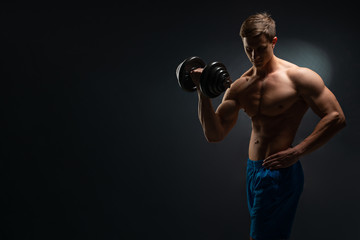 Obraz na płótnie Canvas Handsome power athletic man in training swap muscles with dumbbells. A strong six-pack bodybuilder, perfect abs, shoulders, biceps, triceps and chest. On a dark background under the banner