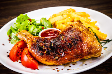 Roasted chicken leg with french fries and vegetable salad on wooden background