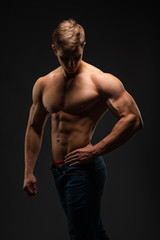 Fototapeta na wymiar young, Strong bodybuilder with six packs. Bodybuilder flexes muscles against dark background