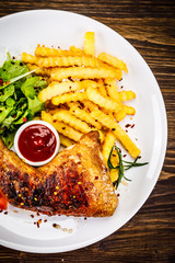 Roasted chicken leg with french fries and vegetable salad on wooden background