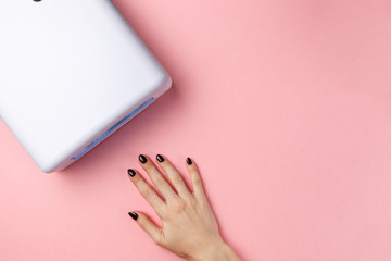 Female hand with manicured nails and UV lamp lights for nails on pink background. Top view. Flat lay. Copy space. Minimal creative concept. Pink background in pastel colours