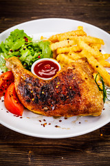 Roasted chicken leg with french fries and vegetable salad on wooden background