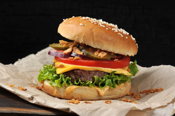 Cheeseburger on craft paper. Dried onions are scattered around the cheeseburger. Black background. Close-up. Macro shooting.