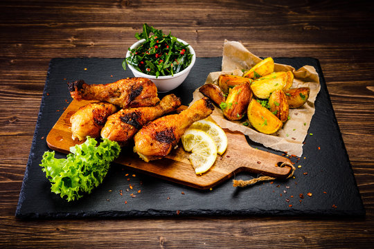 Grilled chicken drumsticks with baked potatoes and vegetable salad on wooden table