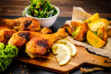 Grilled chicken drumsticks with baked potatoes and vegetable salad on wooden table