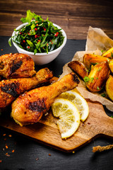 Grilled chicken drumsticks with baked potatoes and vegetable salad on wooden table