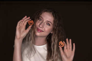 Beautiful young playful funny woman posing isolated over dark beige background wall holding pumpkin halloween glitter decor in hands.