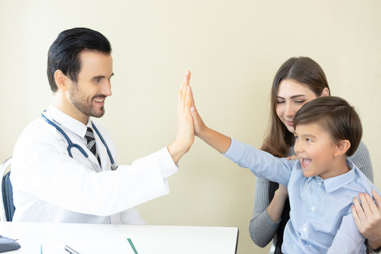 Little boy with his mother at a doctor on consultation. Male doctor is smiling and giving high five to little boy after medical checkup.Concept of healthcare, medical treatment and insurance.