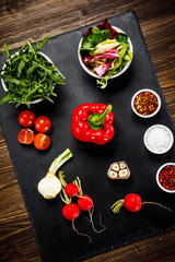Ingredients for vegetable salad on black stone plate on wooden background