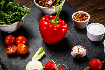 Ingredients for vegetable salad on black stone plate on wooden background