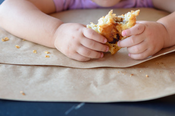 Kid devours croissant or bun roll chocolate .Close up hand Little girl having breakfast in cafe on the city street. The child is eating a croissant. Breakfast black table in restaurant eco paper bag.