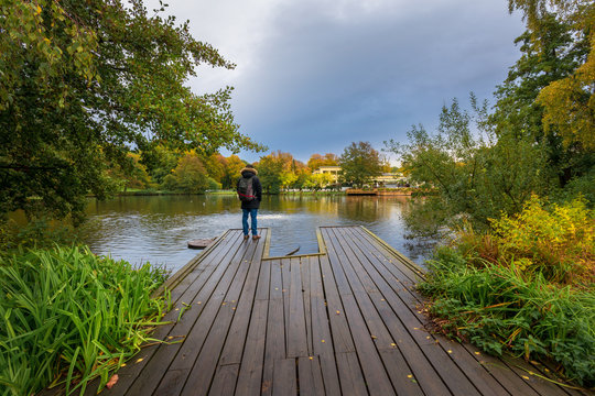 Young adult male on a Jetty leading into lake covered with colorful trees