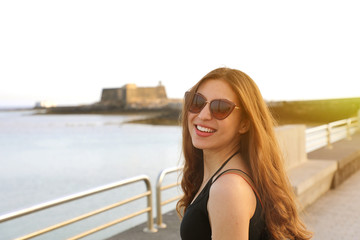 Young pretty smiling woman in black tank top and sunglasses at sunset - obrazy, fototapety, plakaty