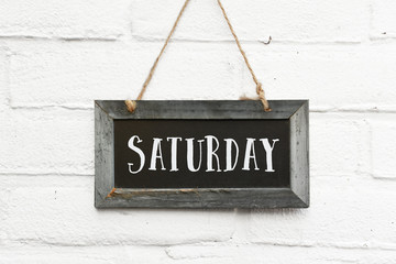 Hello saturday finally weekend text on hanging board white brick outdoor wall