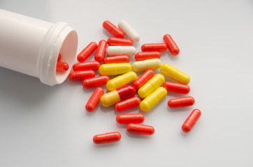 Red capsules pill spilled out of white plastic bottle. Global healthcare concept. Antibiotics drug...