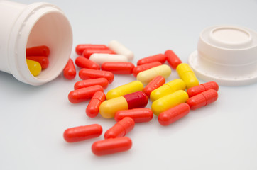 Red capsules pill spilled out of white plastic bottle. Global healthcare concept. Antibiotics drug...