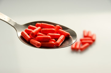 red capsules on a spoon, tablets scattered on a table