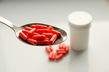red capsules on a spoon, tablets scattered on a table