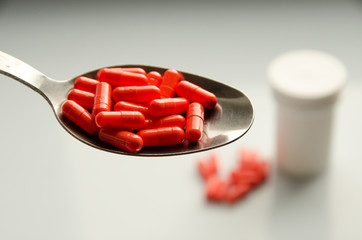 red capsules on a spoon, tablets scattered on a table