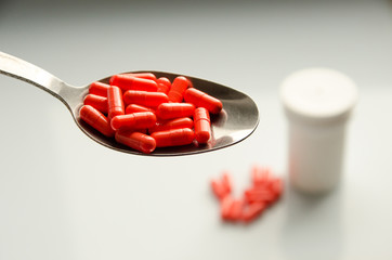 red capsules on a spoon, tablets scattered on a table