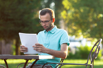 Young man reads documents in street cafe