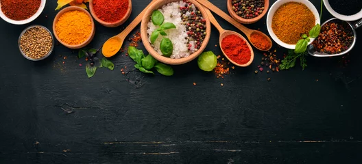 Foto auf Alu-Dibond Gewürze und Kräuter auf einem Holzbrett. Pfeffer, Salz, Paprika, Basilikum, Kurkuma. Auf einer schwarzen Holztafel. Ansicht von oben. Freier Kopienraum. © Yaruniv-Studio