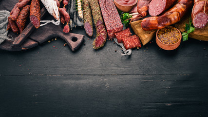 Assortment of salami and snacks. Sausage Fouet, sausages, salami, paperoni. On a black wooden background. Top view. Free space for your text.