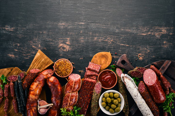 Assortment of salami and snacks. Sausage Fouet, sausages, salami, paperoni. On a black wooden...