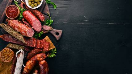 Assortment of salami and snacks. Sausage Fouet, sausages, salami, paperoni. On a black wooden background. Top view. Free space for your text. - obrazy, fototapety, plakaty