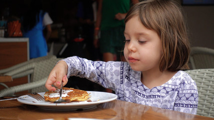 Girl eats pancakes, poured with chocolate and sprinkled with powdered sugar.