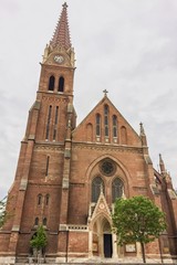 Fototapeta premium Christian church with bell tower, christian church with red bricks on a cloudy sky background, clock tower with a spire