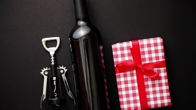 Red wine bottle, corkscrew and boxed christmas gift on black matte background. Top view with copy space