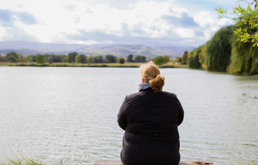 Frau sitzt nachdenklich an einem See