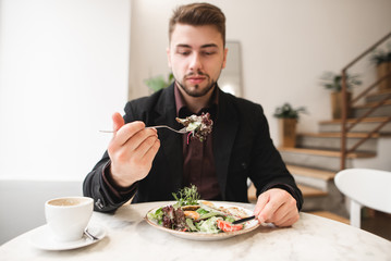 Attractive man with a beard eating a diet salad in a cozy restaurant. Man took the green salad on the fork. Focus on the green on the fork. Good food.