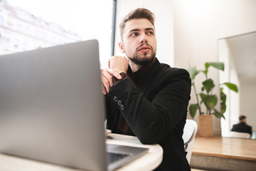 Portrait of a busy business man sitting in a cafe with a laptop. Man in a suit works on a computer in a cozy light restaurant.