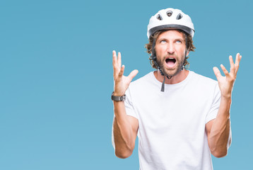 Handsome hispanic cyclist man wearing safety helmet over isolated background crazy and mad shouting...
