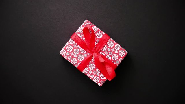 Gift box wrapped with red snow flakes pattern christmas paper with red bow on black table, top view