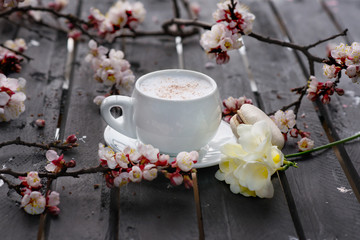 Cup of hot  coffee with macaroon cookies and spring flowers on the old rustic black wooden tabletop.